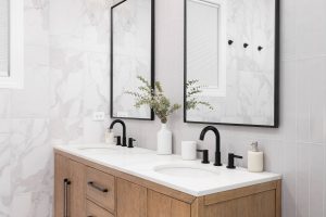 A bathroom with white marble countertop and a white oak vanity cabinet. the sink has a black faucet and two mirrors with black frames around them.