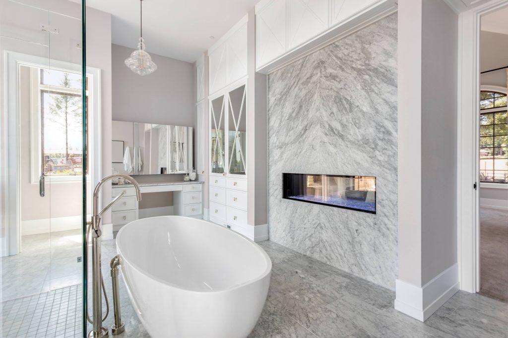 bathroom remodeling in Santa Cruz, California. the bathroom is made using light colors and white and gray marble. the bathroom has a white tub and a built in fire place.